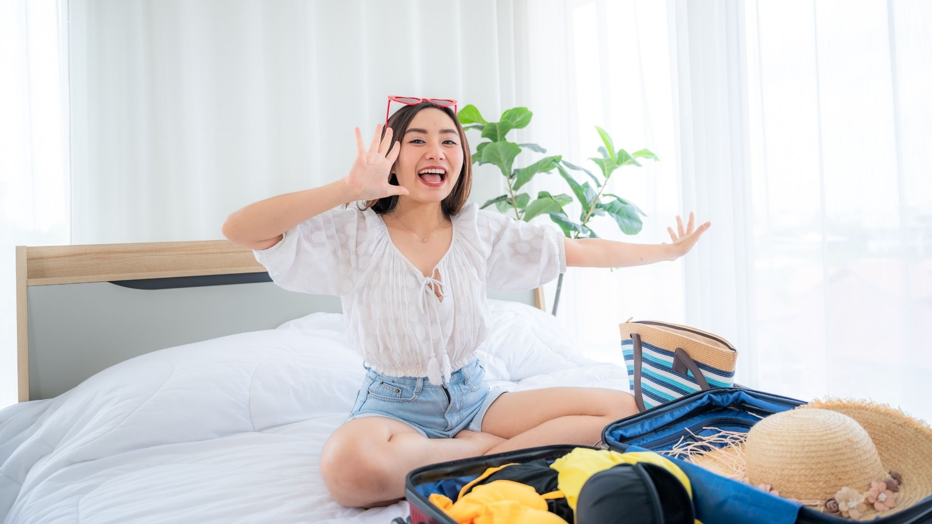 A female hotel guest smiling happily in her hotel bedroom, surrounded by her travel bags.