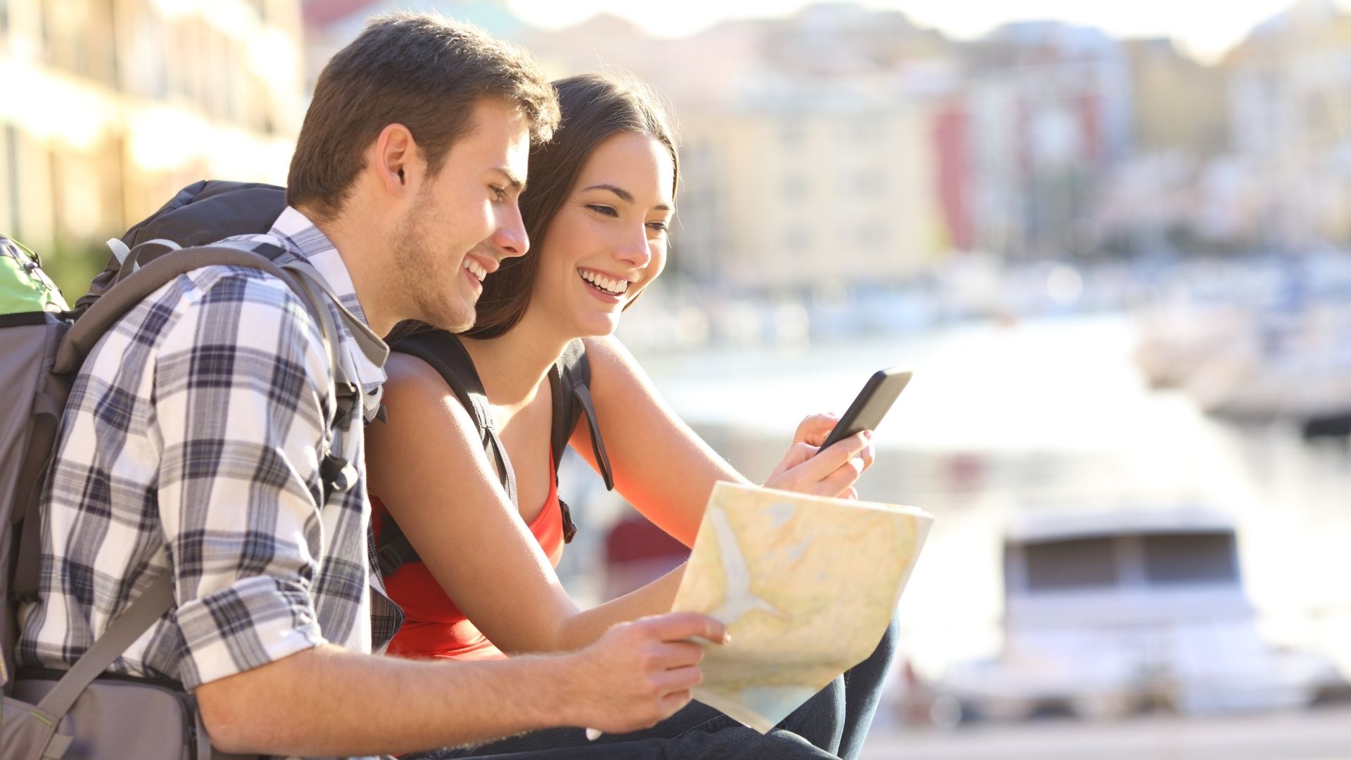A happy traveler couple enthusiastically exploring their destination using maps and smartphones.
