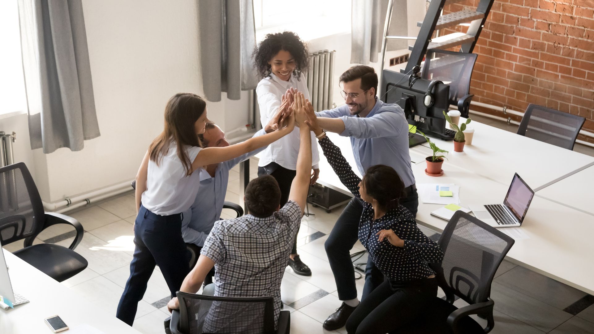 A group of six digital marketing team members celebrating the success of their campaign with high fives in the office.