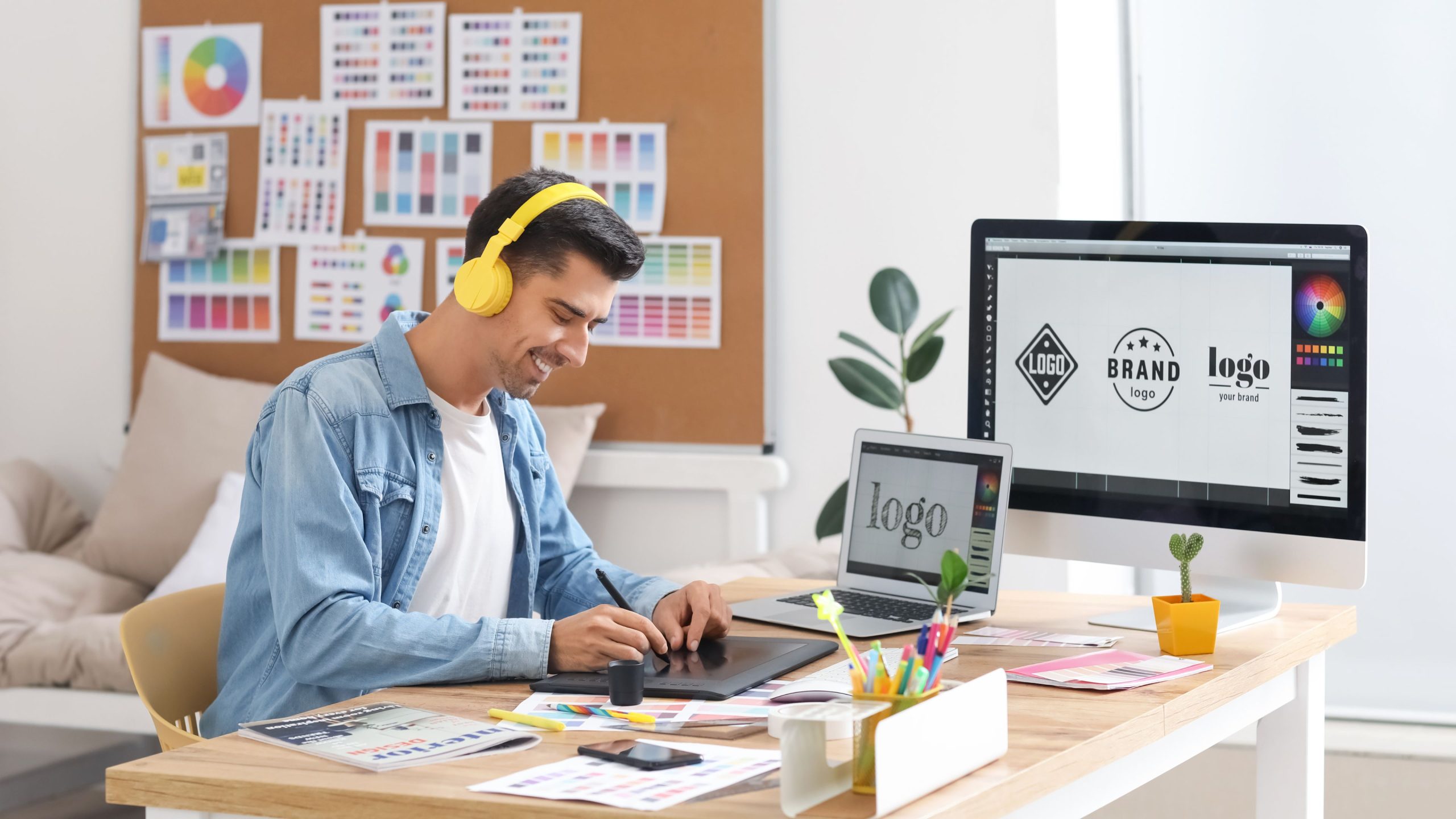Male graphic designer happily wearing yellow headphones, creating logo design for client