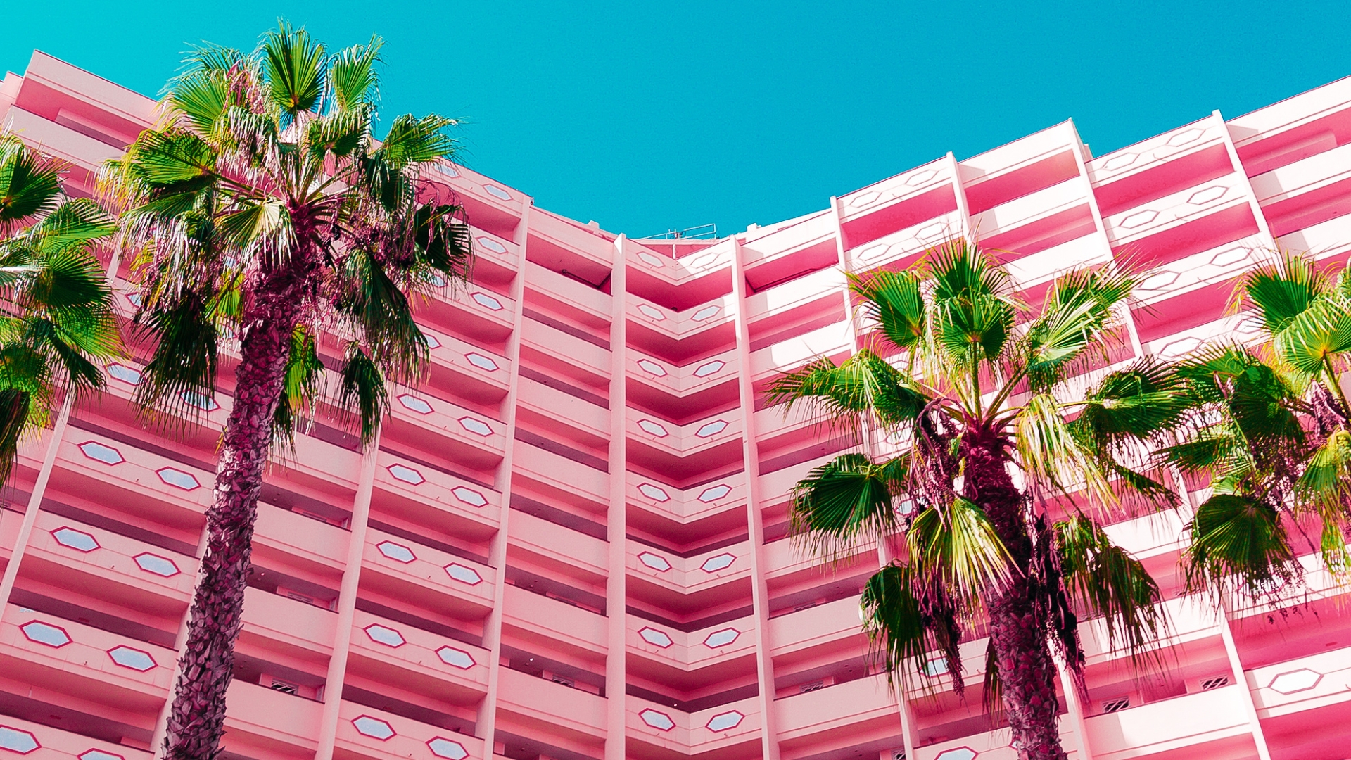Big building of luxury hotel in pink with two palm trees