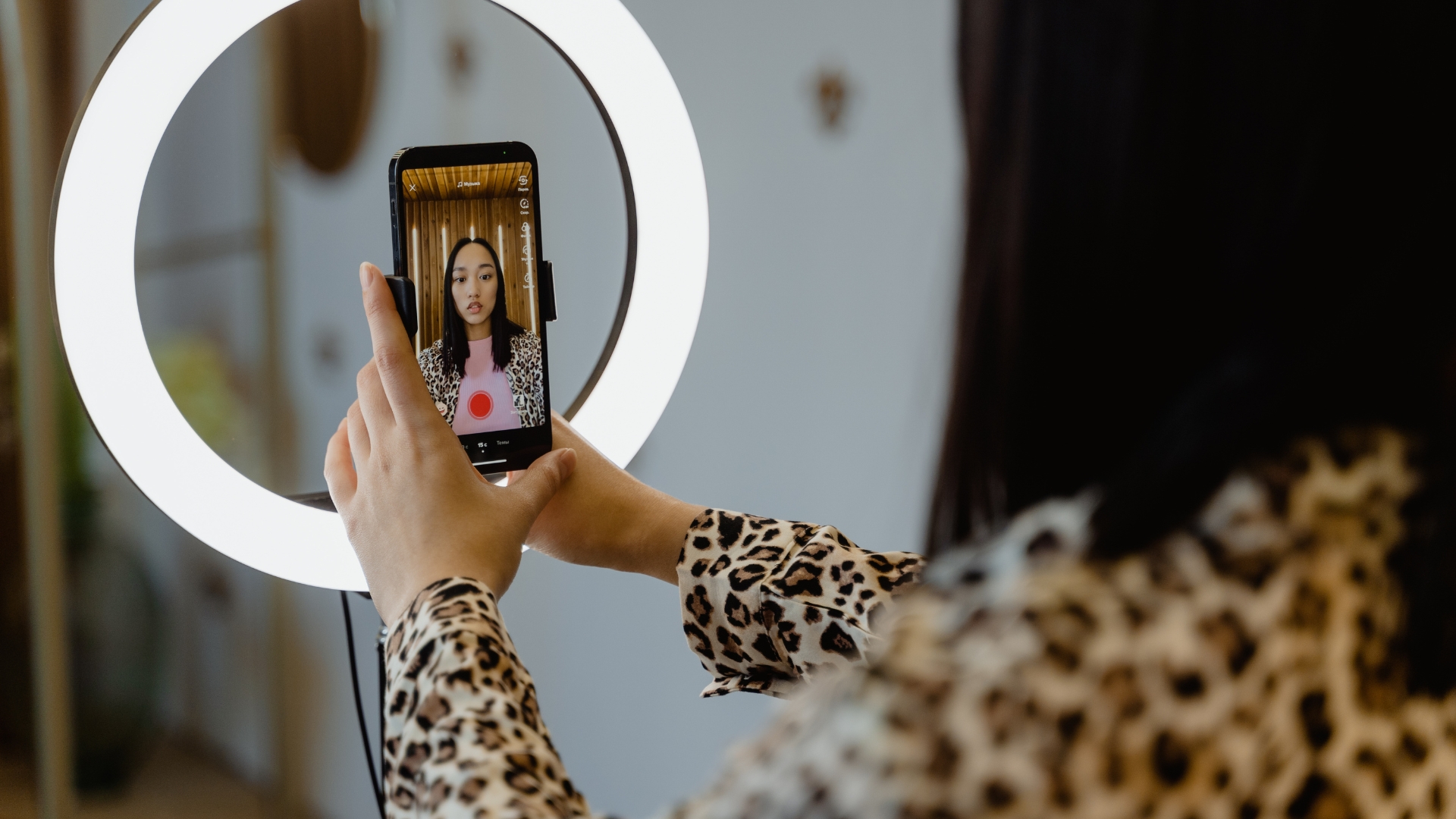 A female influencer wearing a leopard dress is creating engaging trendy content using her cellphone with the help of ringlight on the TikTok app.
