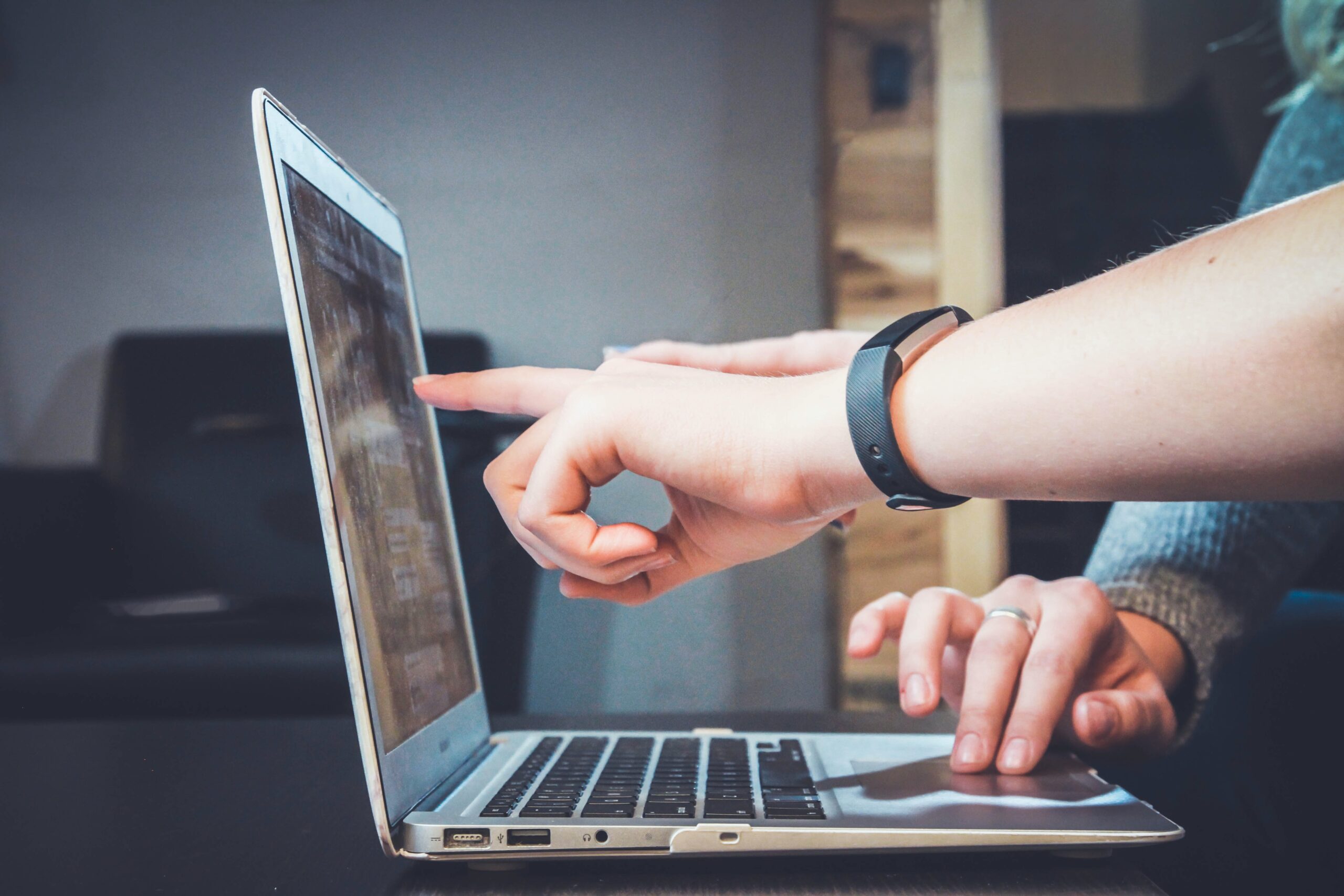 A man wearing a black wristband is pointing at a laptop screen about linked advertising that needs to be fixed and a woman wearing a silver ring on her ring finger as an ad maker agrees.