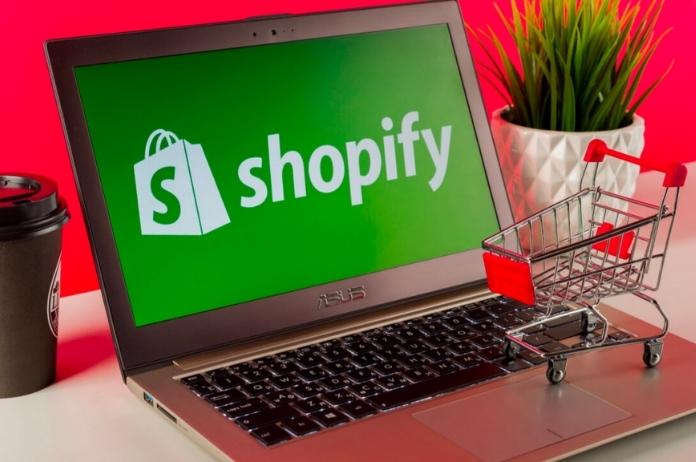 Black laptop displaying Shopify logo with shopping cart miniature on the top of it