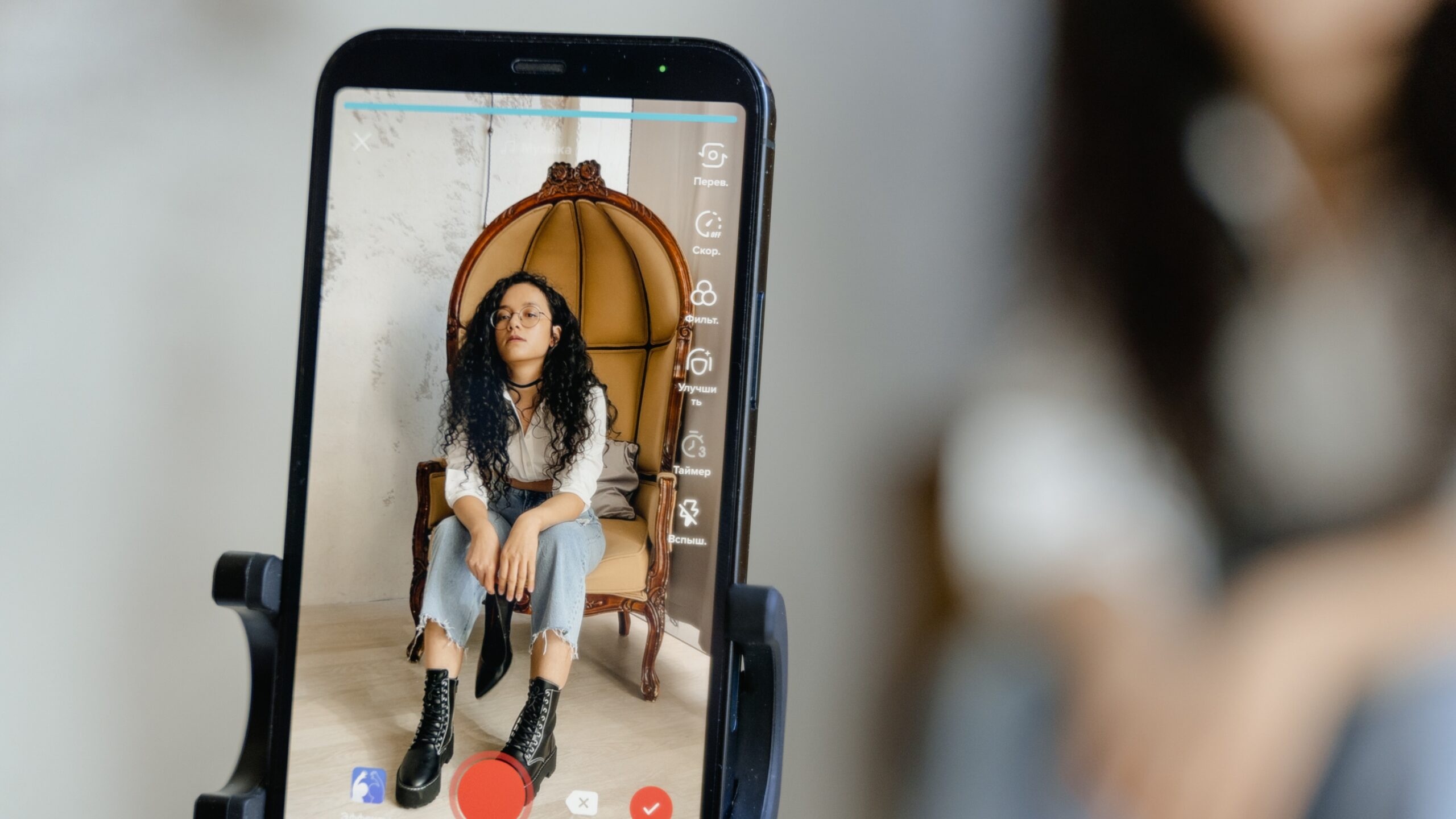 Female marketer doing TikTok live marketing by posing on the chair while facing the phone's camera