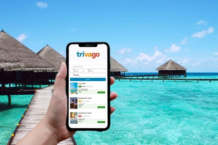 Male traveler holding a black smartphone displaying the Trivago application on the hotel beach