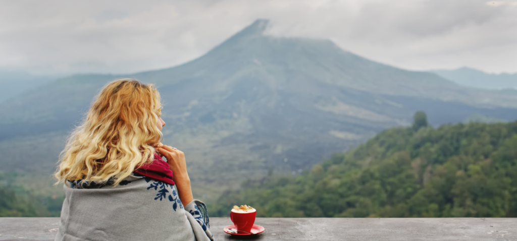 Wanita sedang minum kopi dengan pemandangan gunung agung
