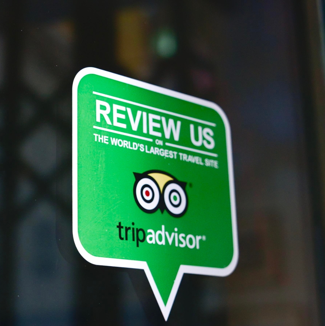 a green sticker with a word of review us in white color and tripadvisor logo that stick on the glass