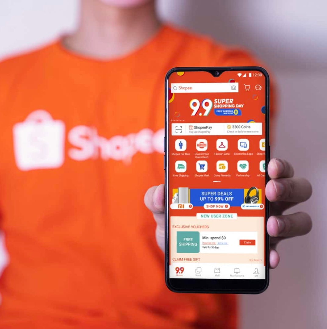 a man with shopee t-shirt shows his phone to the camera that is displaying shopee optimization advertising