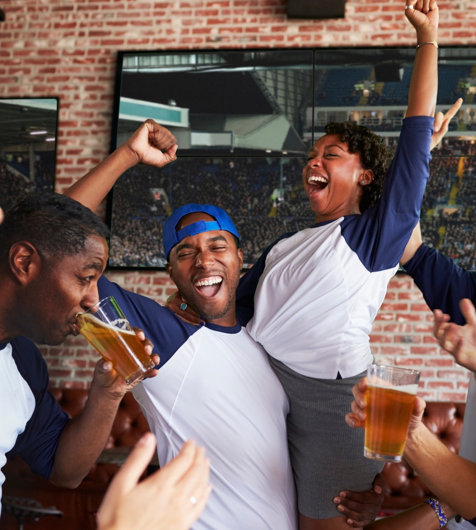 The group is happily celebrating their favorite team's win at a sports bar carrying beers